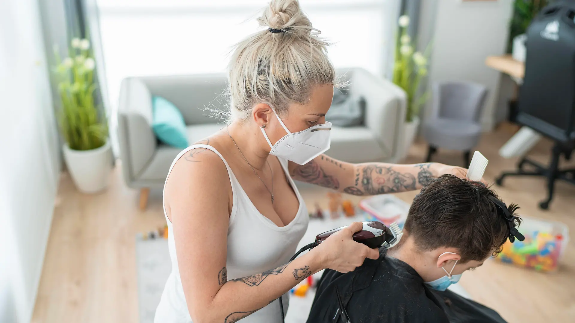 Female hairdresser wearing mask cutting boy s hair with electric razor at home during curfew model released Symbolfoto property released SNF00367