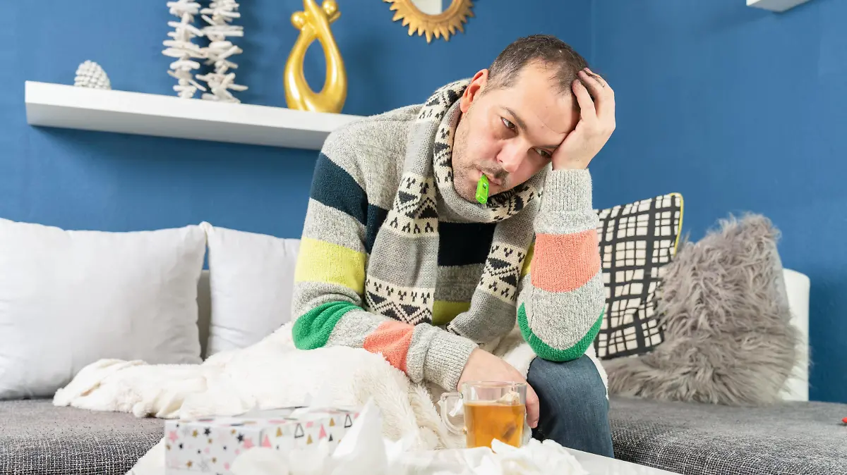 sick man has a clinical thermometer in his mouth and is sitting on his couch Copyright: xjensrotherx Panthermedia28176594 ,model released, Symbolfoto