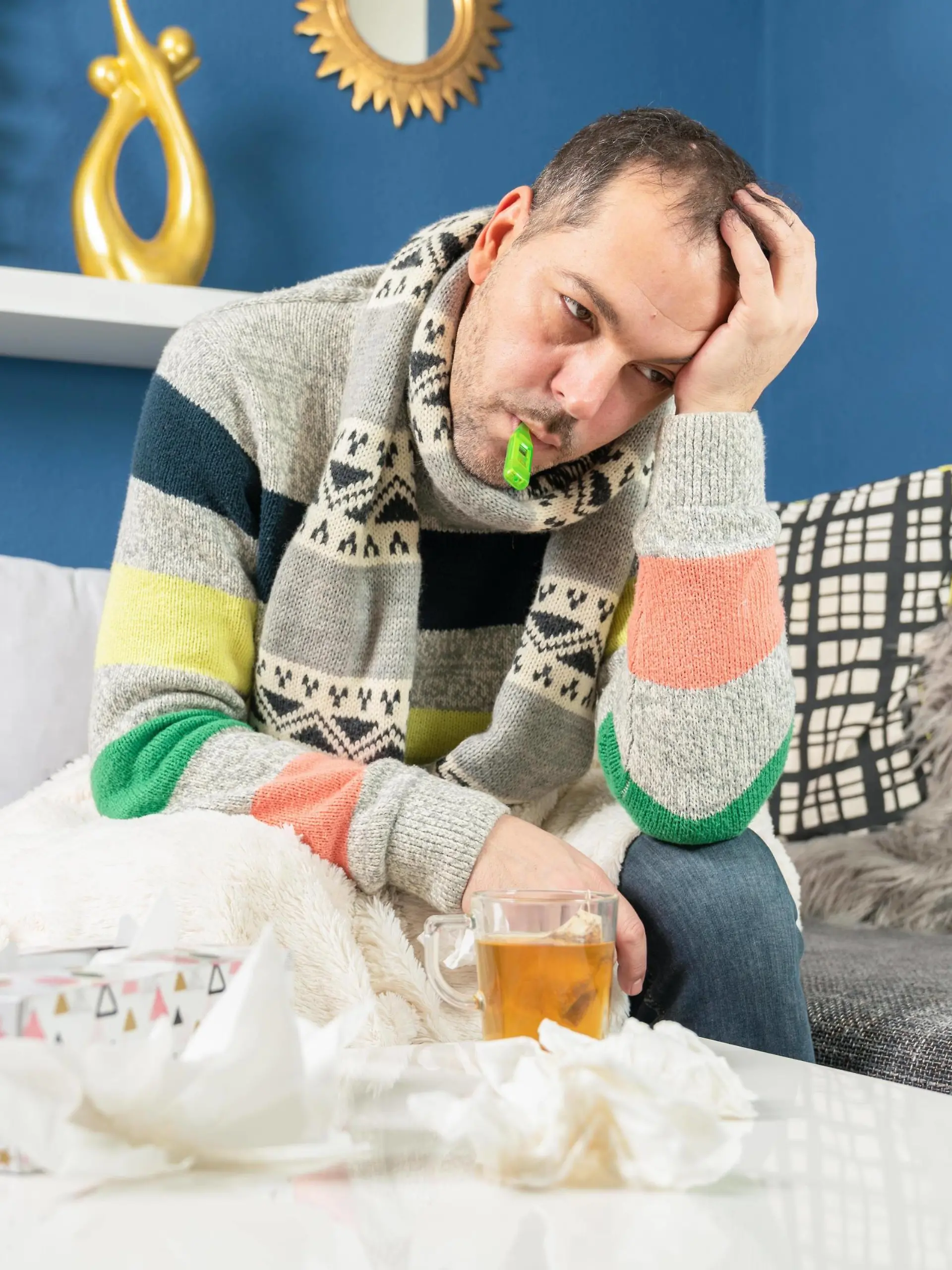 sick man has a clinical thermometer in his mouth and is sitting on his couch Copyright: xjensrotherx Panthermedia28176594 ,model released, Symbolfoto