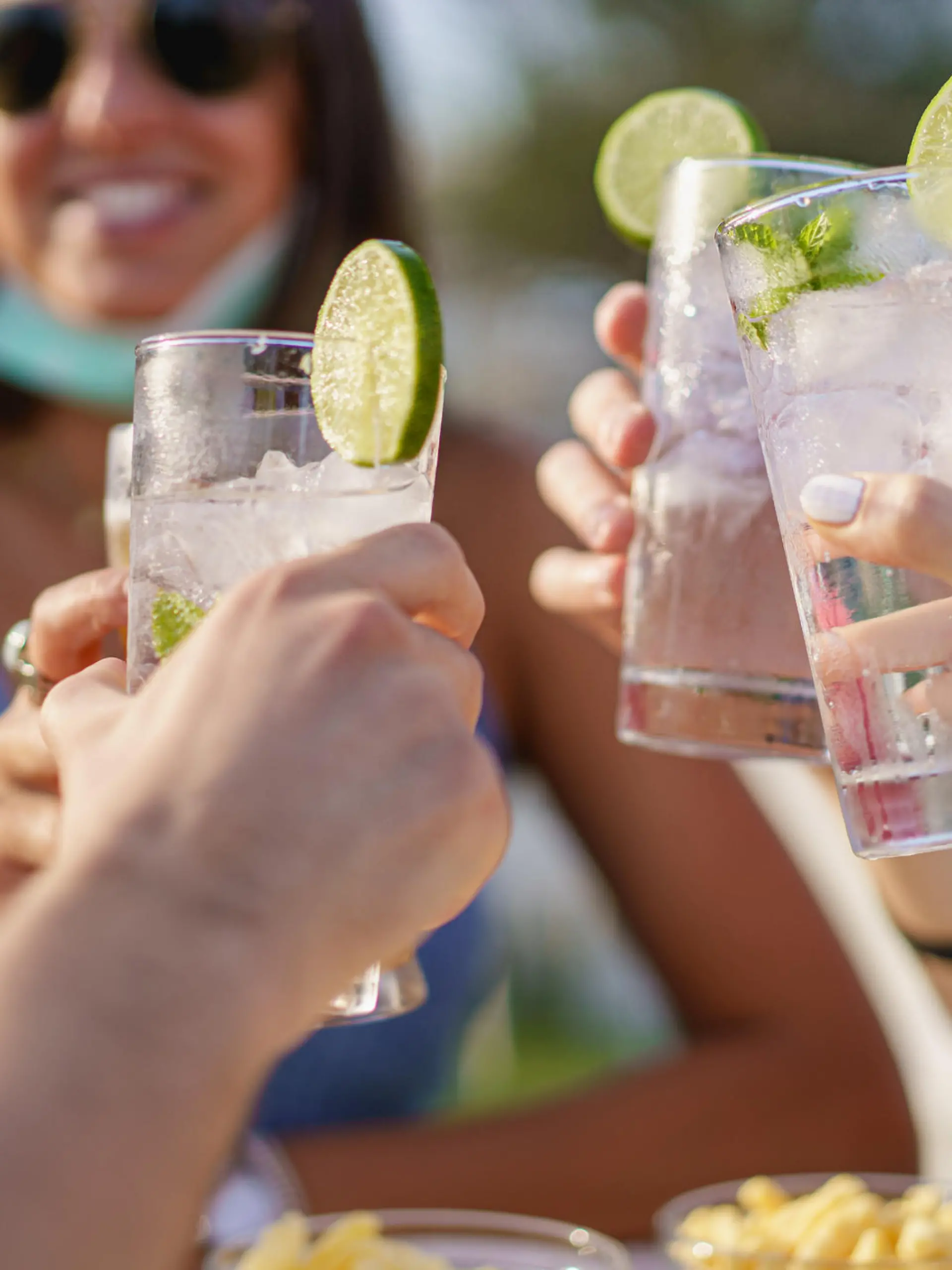 Friends drinking cocktails in an outdoors snack bar restaurant in the summer wearing face mask on to be protected from coronavirus - Happy people cheering with mojito and having fun (Friends drinking cocktails in an outdoors snack bar restaurant in t