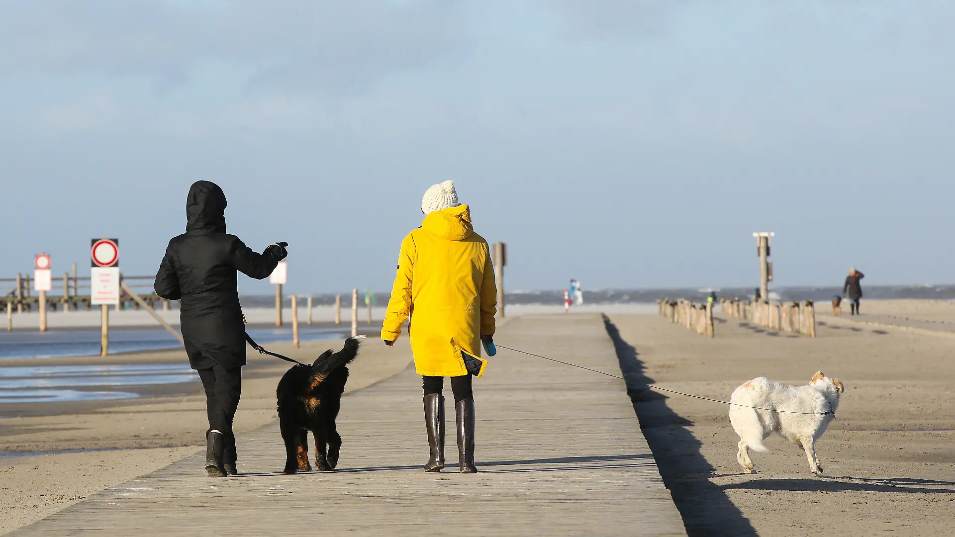 21.01.2021, Schleswig-Holstein, St. Peter Ording: Passanten sind bei Sonne und stürmischem Wetter an der Nordsee in St. Peter Ording unterwegs. Ein Orkantief bringt laut Deutschem Wetterdienst (DWD) am 21.01.2021 besonders an die Nordseeküste schwere Sturmböen. Foto: Bodo Marks/dpa +++ dpa-Bildfunk +++