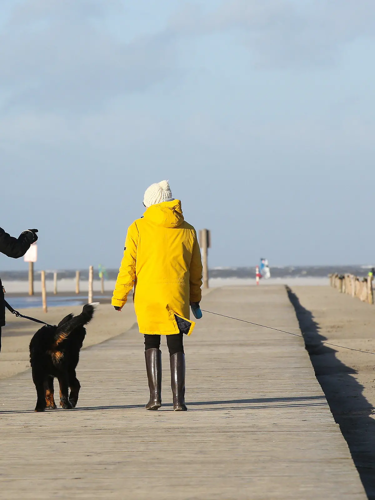 21.01.2021, Schleswig-Holstein, St. Peter Ording: Passanten sind bei Sonne und stürmischem Wetter an der Nordsee in St. Peter Ording unterwegs. Ein Orkantief bringt laut Deutschem Wetterdienst (DWD) am 21.01.2021 besonders an die Nordseeküste schwere Sturmböen. Foto: Bodo Marks/dpa +++ dpa-Bildfunk +++