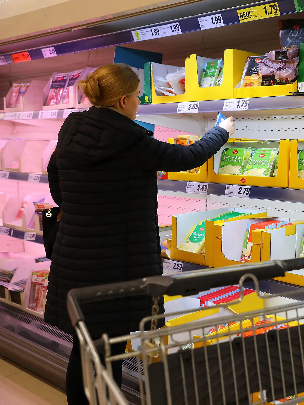 Die aktuelle Inflationsrate kommt auch im Supermarkt an, wo für die Bürgerinnen und Bürger vieles teurer wird. Eine Frau steht an der Kühltheke und vergleicht die Preise.