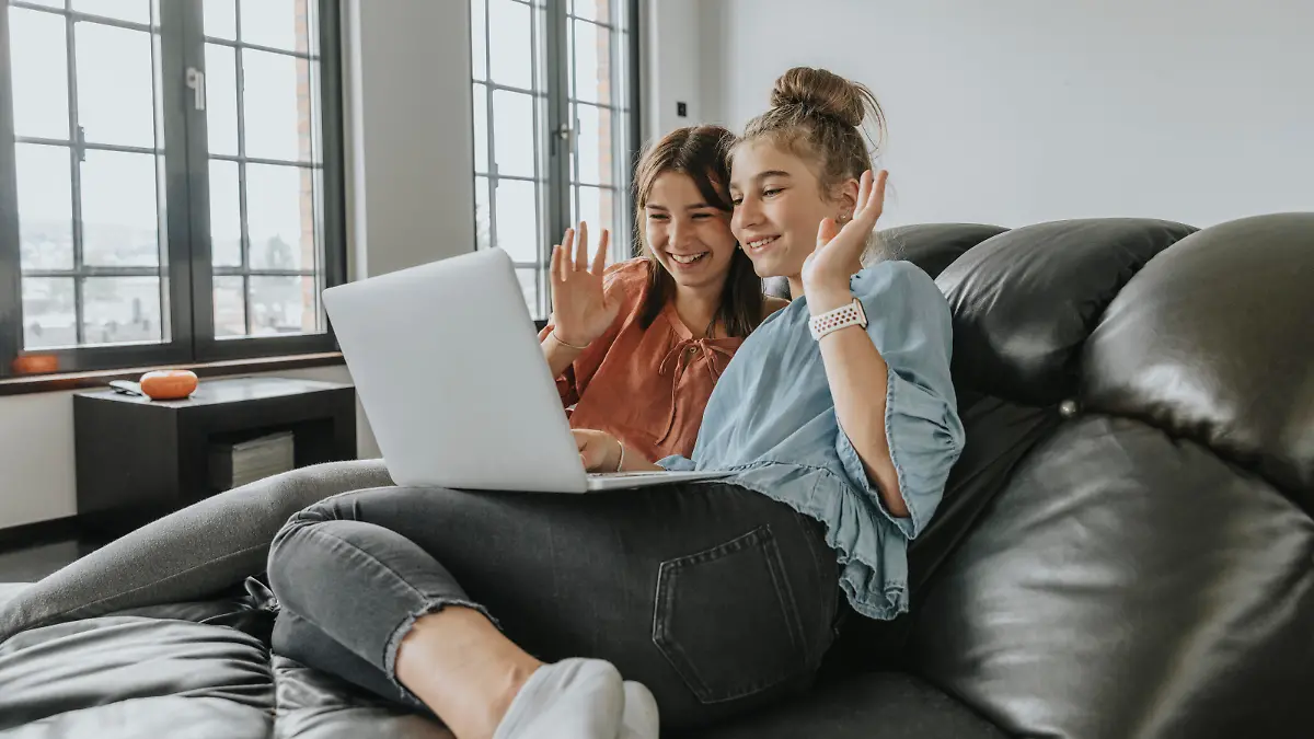  Friends waving while video conferencing over laptop on sofa at home model released Symbolfoto property released MFF06109