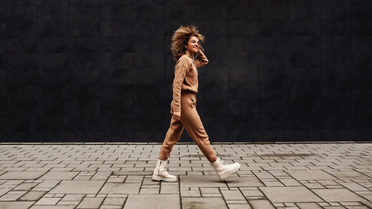 Young fashionable woman with curly hair walking on the street and listening to the music.