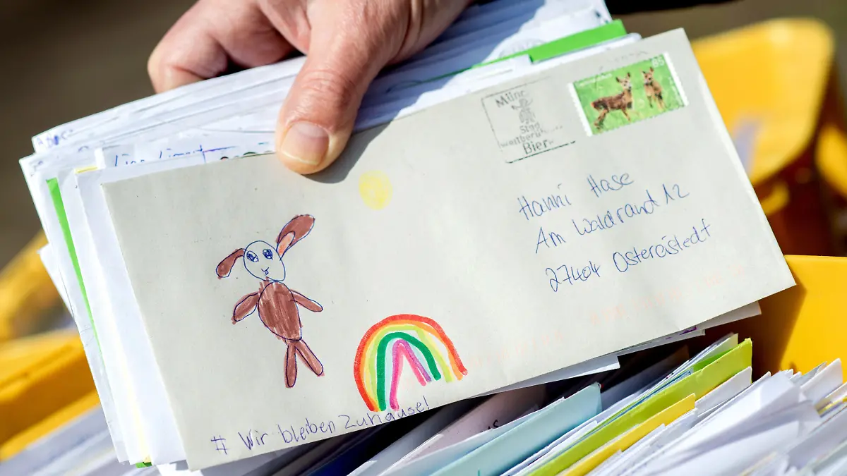 ARCHIV - 09.04.2020, Niedersachsen, Ostereistedt: Ein Mitarbeiter des Osterpostamts hält vor dem Gemeindehaus von Ostereistadt einen Brief in den Händen, der einen gemalten Regenbogen und die Aufschrift «Wir bleiben Zuhause!» zeigt. Die Briefschreibeaktion findet auch in diesem Jahr wieder statt bis zum 29. März. 2020 ging eine Rekordzahl von etwa 59000 Briefen im Osterpostamt ein. (Zu dpa: «Osterhase in Ostereistedt freut sich wieder auf Kinderbriefe») Foto: Hauke-Christian Dittrich/dpa +++ dpa-Bildfunk +++
