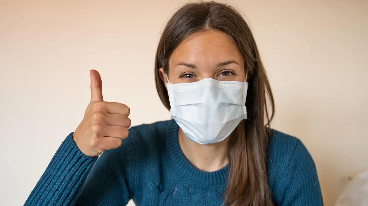 Junge Frau mit OP-Maske hält den Daumen hoch