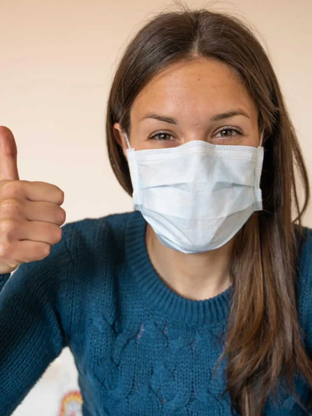 Junge Frau mit OP-Maske hält den Daumen hoch