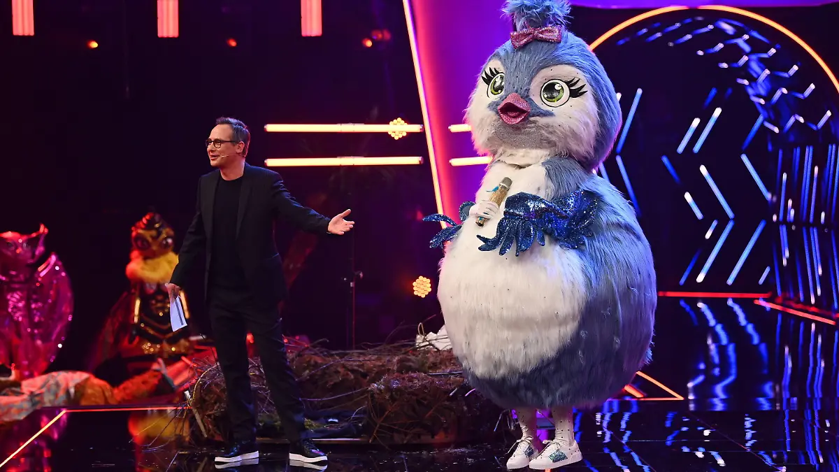 HANDOUT - 16.02.2021, Nordrhein-Westfalen, Köln: Die Figur «Küken» steht in der ersten Folge der vierten Staffel der ProSieben-Show «The Masked Singer» neben Moderator Matthias Opdenhövel auf der Bühne. Bei «The Masked Singer» singen Prominente in aufwendigen Bühnenkostümen um die Wette. Foto: Willi Weber/ProSieben/dpa - ACHTUNG: Nur zur redaktionellen Verwendung im Zusammenhang mit einer Berichterstattung über die Sendung und nur mit vollständiger Nennung des vorstehenden Credits. Das Foto darf nicht verändert und nur im vollen Ausschnitt verwendet werden. Keine Archivierung +++ dpa-Bildfunk +++