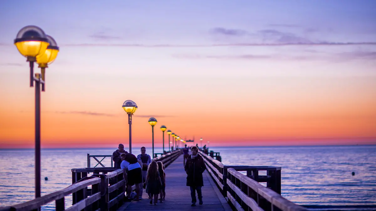 ARCHIV - 24.06.2020, Mecklenburg-Vorpommern, Graal-Müritz: Urlauber sind nach Sonnenuntergang auf der Seebrücke unterwegs. Nach einer wegen der Corona-Pandemie völlig vermurksten Saison steht für die Tourismusbranche nun im Herbst der Endspurt an. (zu dpa «Tourismusbranche hofft auf Endspurt im Herbst») Foto: Jens Büttner/dpa-Zentralbild/dpa +++ dpa-Bildfunk +++
