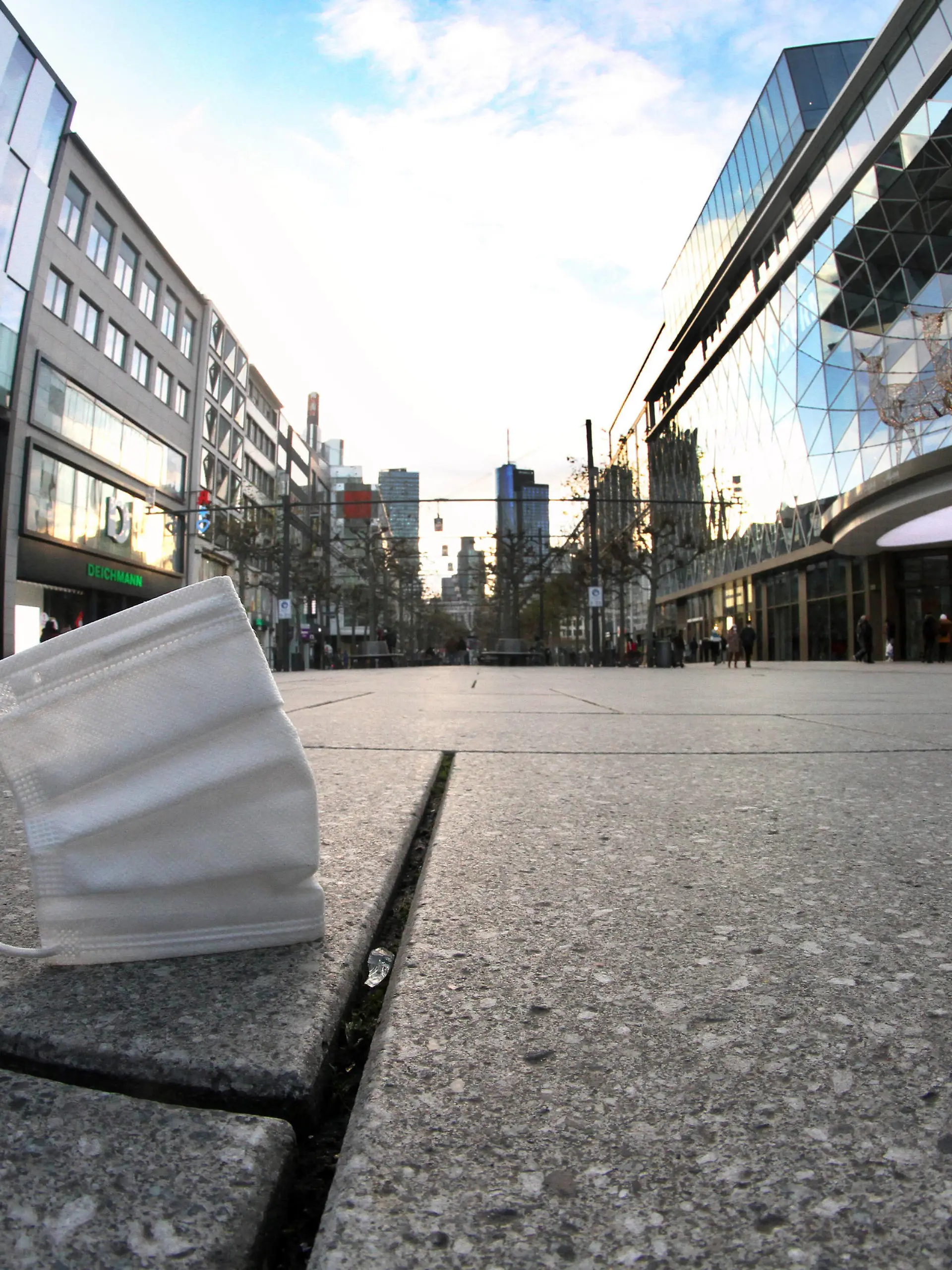 Getragene Mund-Nase-Bedeckungsmaske liegt auf dem Pflaster der menschenleeren Fußgängerzone und Einkaufsstraße Zeil in der Innenstadt von Frankfurt, Hessen, Deutschland *** Worn mouth nose covering mask lies on the pavement of the deserted pedestrian zone and shopping street Zeil in downtown Frankfurt, Hesse, Germany 