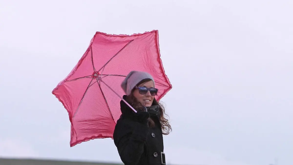 junge Frau mit rosa Schirm balanciert ueber Buhnen, Leuchtturm im Hintergrund, Niederlande, Zeeland, Breskens | young woman with pink umbrella balancing on spur dikes with lighthouse in the background, Netherlands, Zeeland, Breskens | Verwendung weltweit