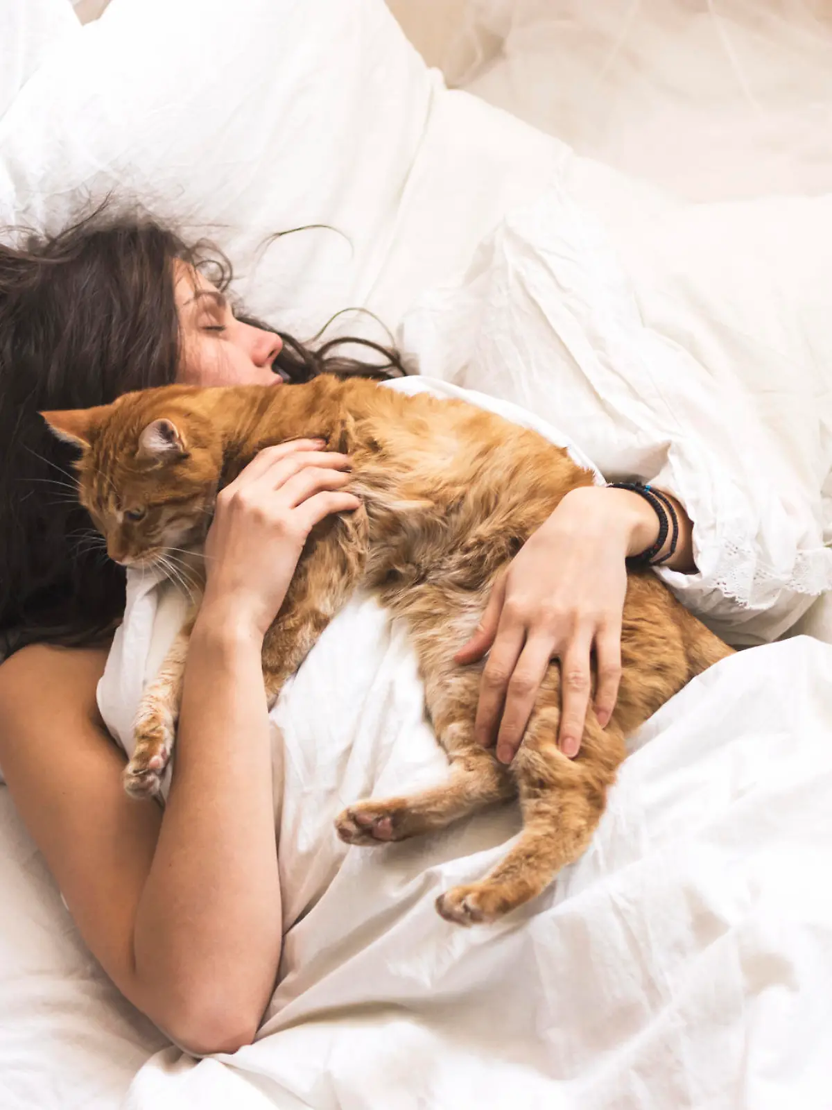 Frau schläft mit Katze im Bett.