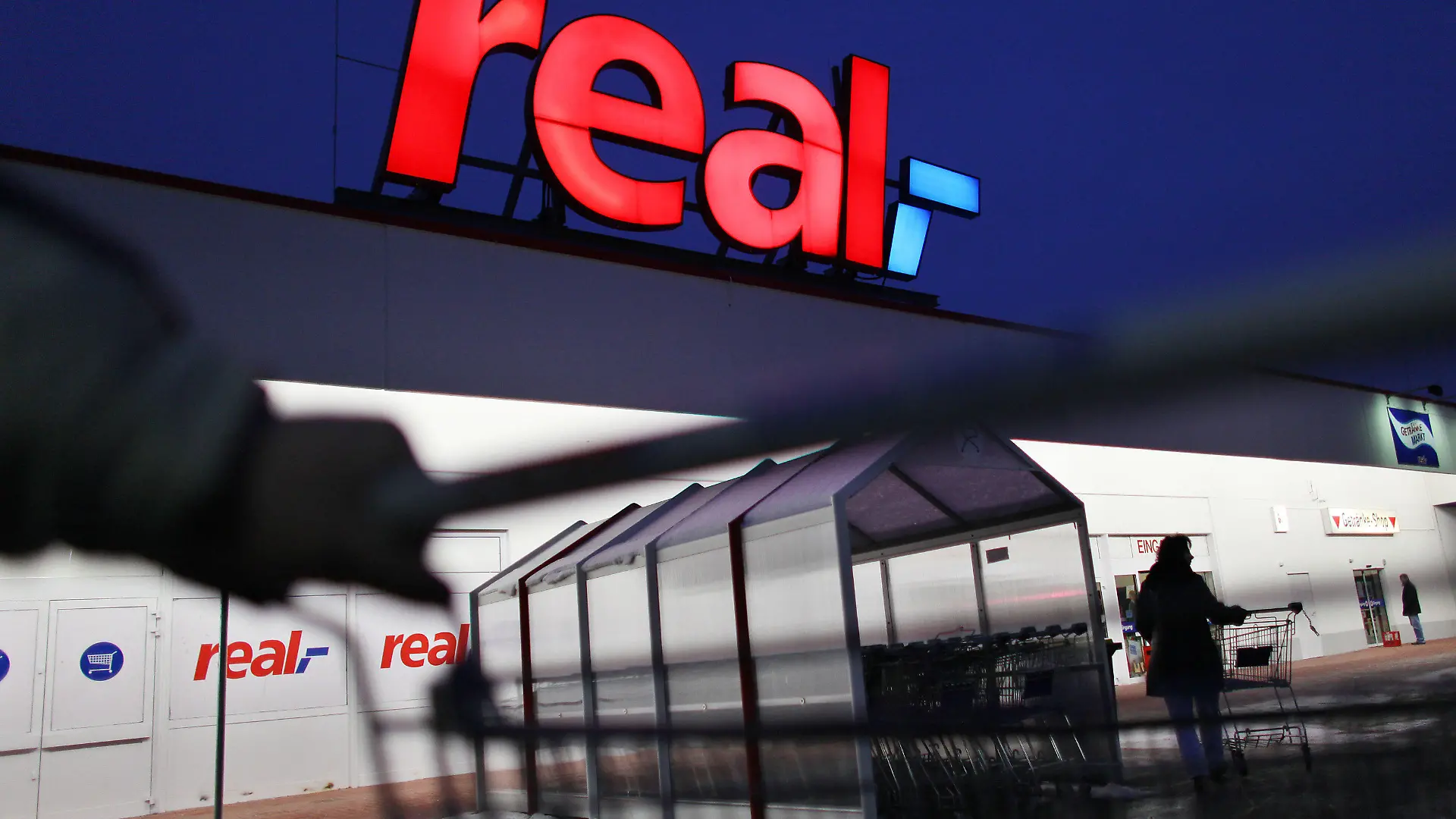 ARCHIV - Ein Mann schiebt seinen Einkaufswagen vor einem Real Supermarkt in Köln (Foto vom 12.01.2010). Wichtige Markenhersteller wie Dr. Oetker beliefern die Supermarktkette derzeit nicht. Es gibt Streit um die Konditionen. Wenn es ums Geld geht, wird im Handel öfter mit harten Bandagen gekämpft. Foto: Oliver Berg/dpa (zu dpa-KORR: "Lücken im Regal: Real hat Ärger mit Lieferanten" vom 17.07.2015) +++(c) dpa - Bildfunk+++