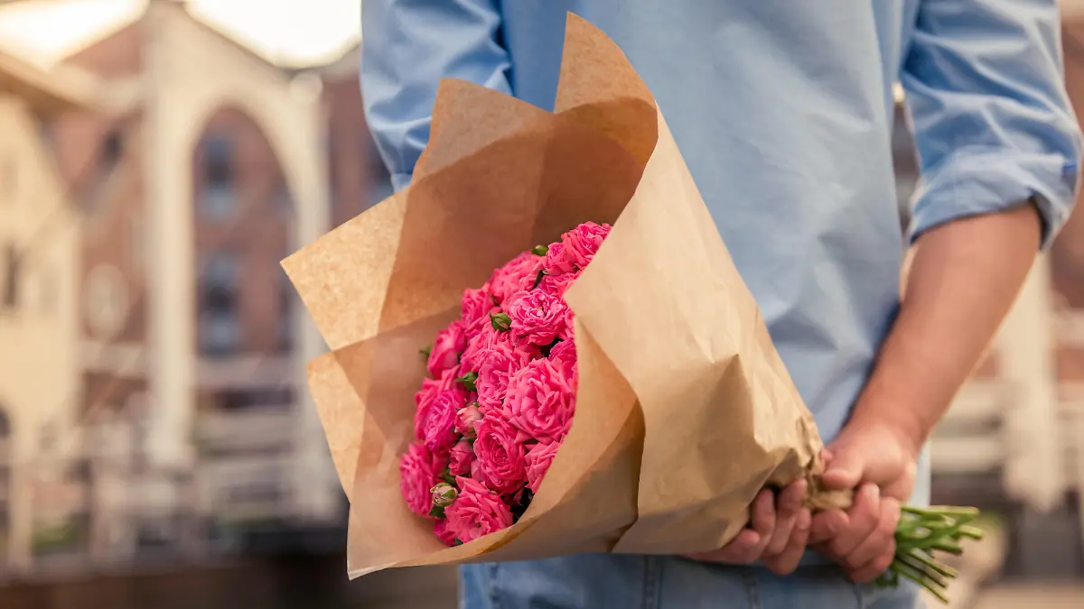 Mann hält einen großen Blumenstrauß hinter dem Rücken.