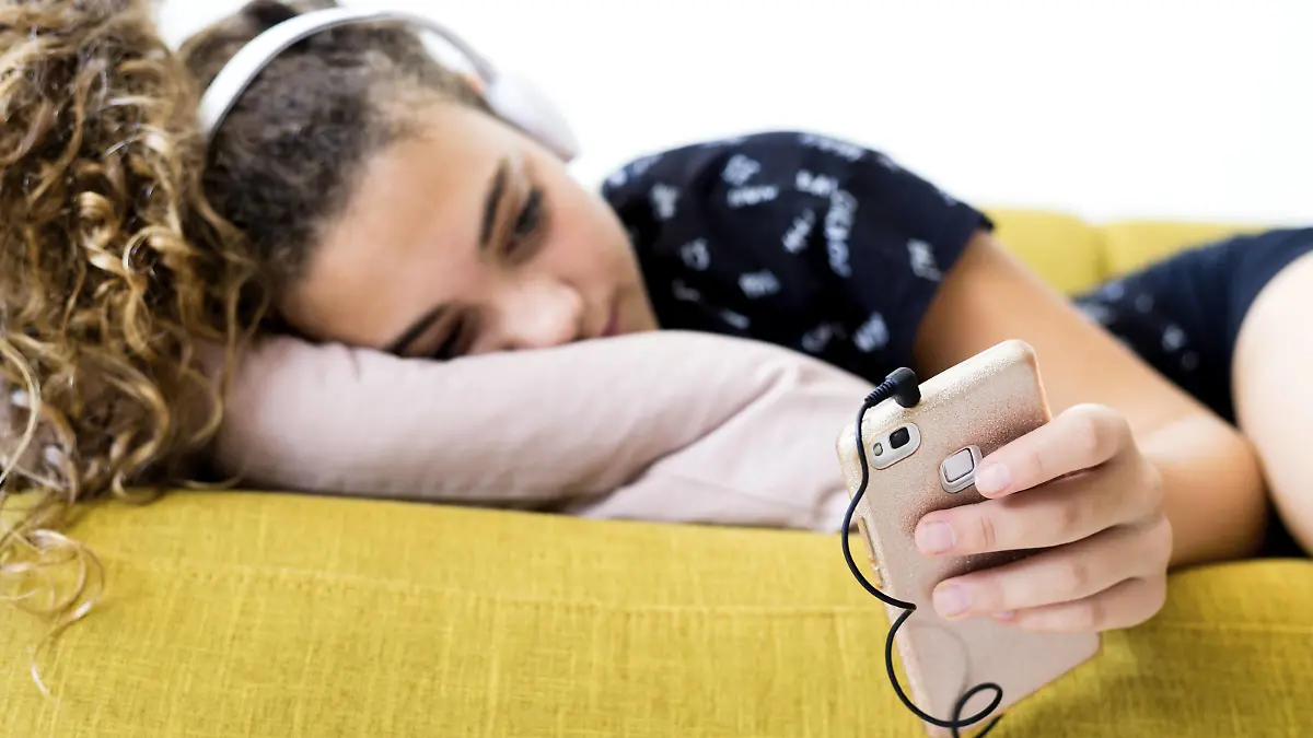 Girl lying on the couch at home listening music with headphones and smartphone model released Symbolfoto property released PUBLICATIONxINxGERxSUIxAUTxHUNxONLY ERRF00053