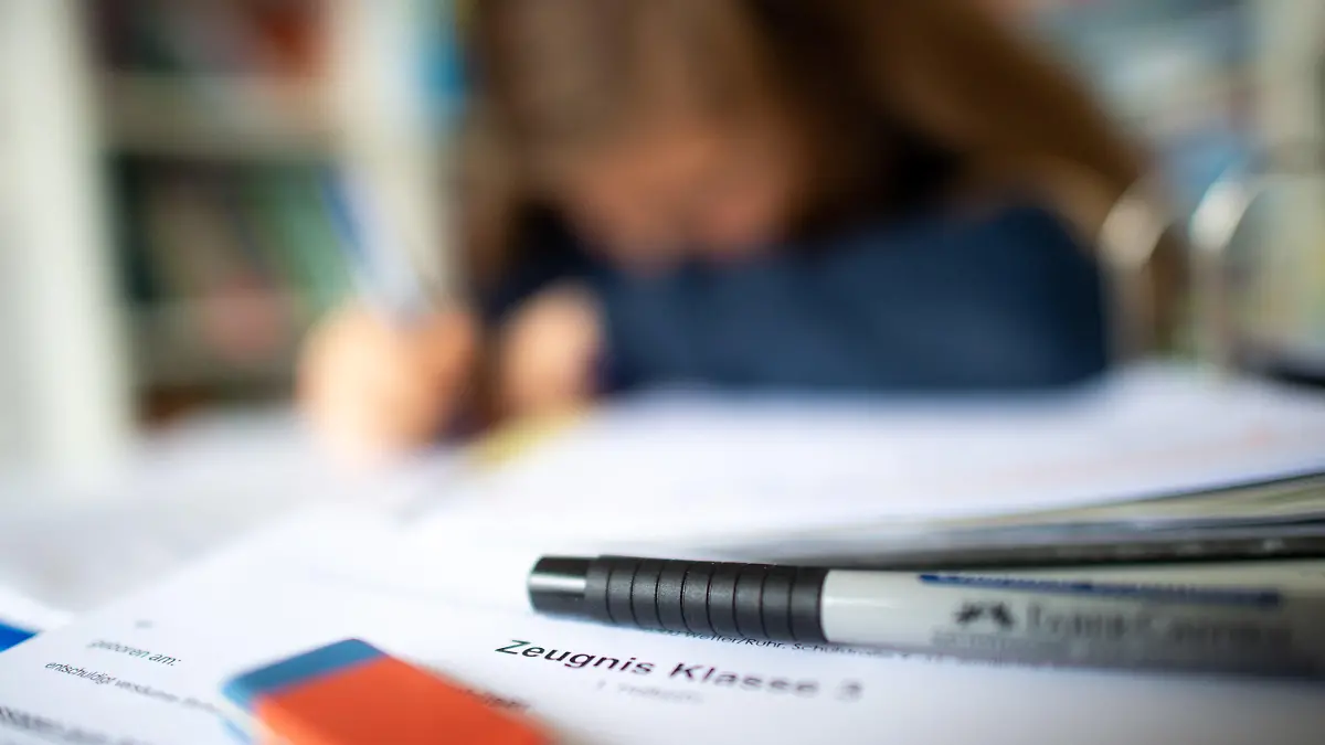29.01.2021, Nordrhein-Westfalen, Wetter: ILLUSTRATION - Eine Schülerin der dritten Klasse arbeitet an ihrem Schreibtisch, während ihr Zeugnis auf ihrem Schreibtisch liegt (gestellte Szene). Mitten im coronabedingten Distanzunterricht erhalten 2,5 Millionen Schüler in Nordrhein-Westfalen ihre Halbjahreszeugnisse. Foto: Jonas Güttler/dpa +++ dpa-Bildfunk +++