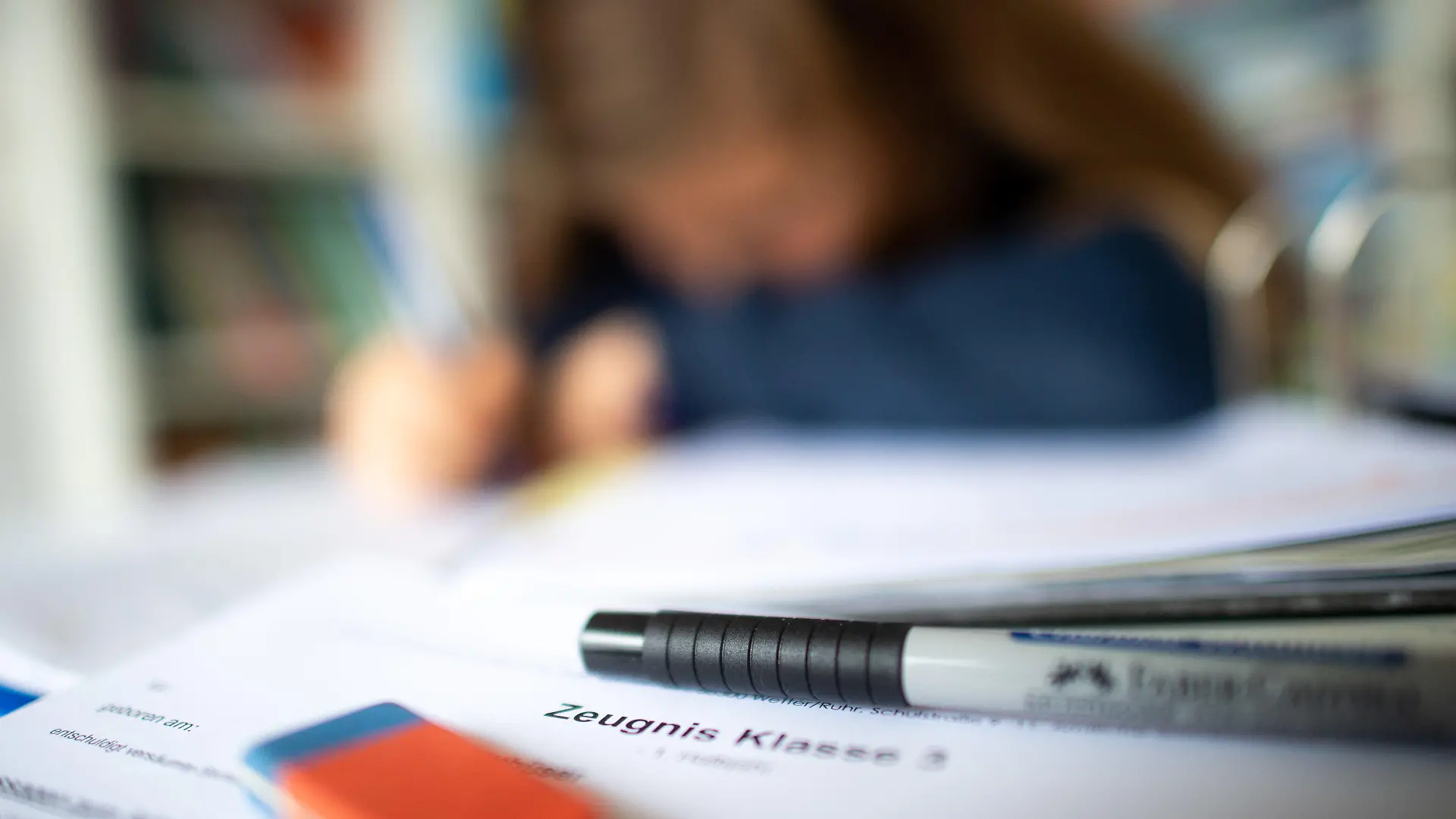 29.01.2021, Nordrhein-Westfalen, Wetter: ILLUSTRATION - Eine Schülerin der dritten Klasse arbeitet an ihrem Schreibtisch, während ihr Zeugnis auf ihrem Schreibtisch liegt (gestellte Szene). Mitten im coronabedingten Distanzunterricht erhalten 2,5 Millionen Schüler in Nordrhein-Westfalen ihre Halbjahreszeugnisse. Foto: Jonas Güttler/dpa +++ dpa-Bildfunk +++