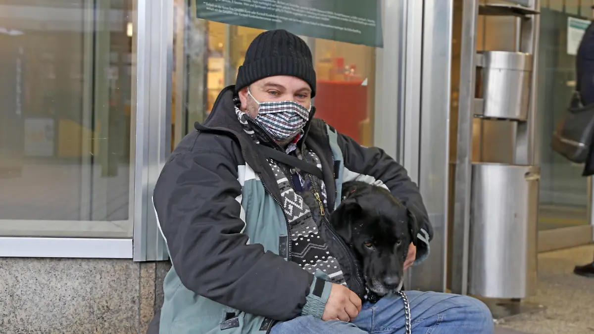 Obdachloser sitzt mit seinem Hund vor einem Geschäft