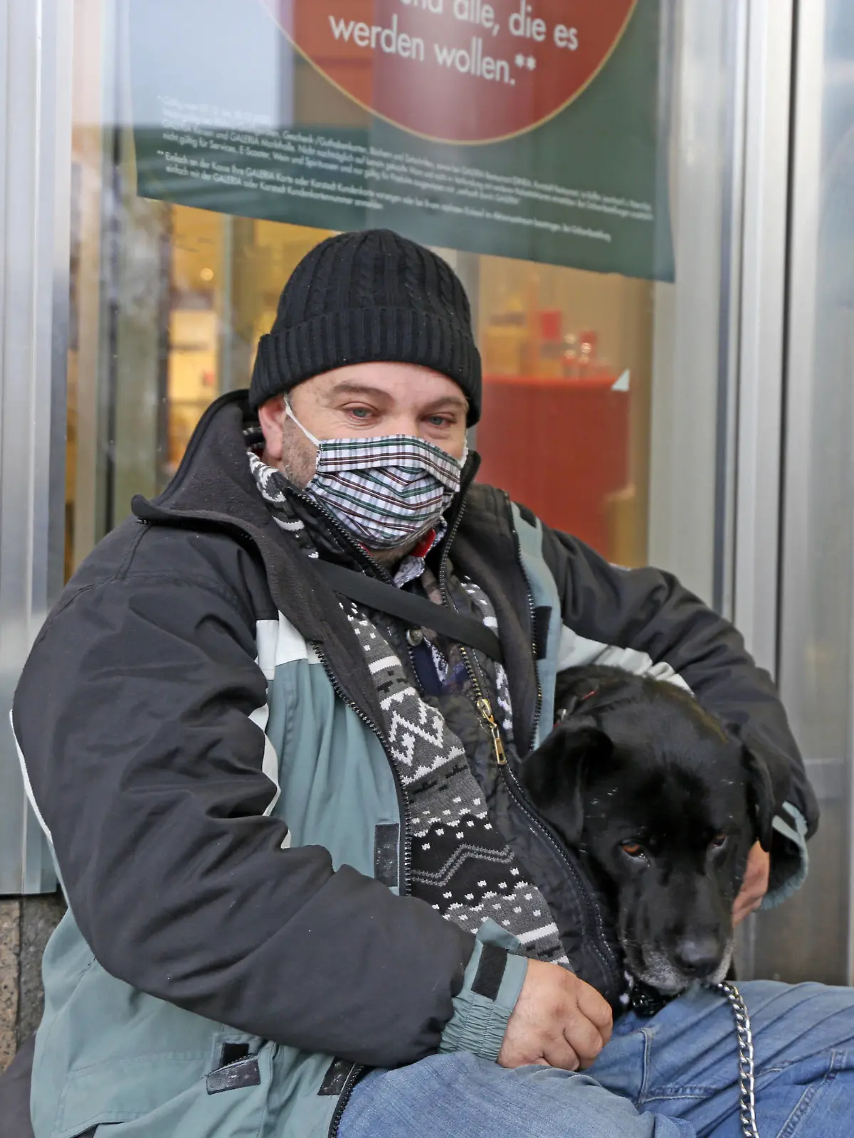 Obdachloser sitzt mit seinem Hund vor einem Geschäft