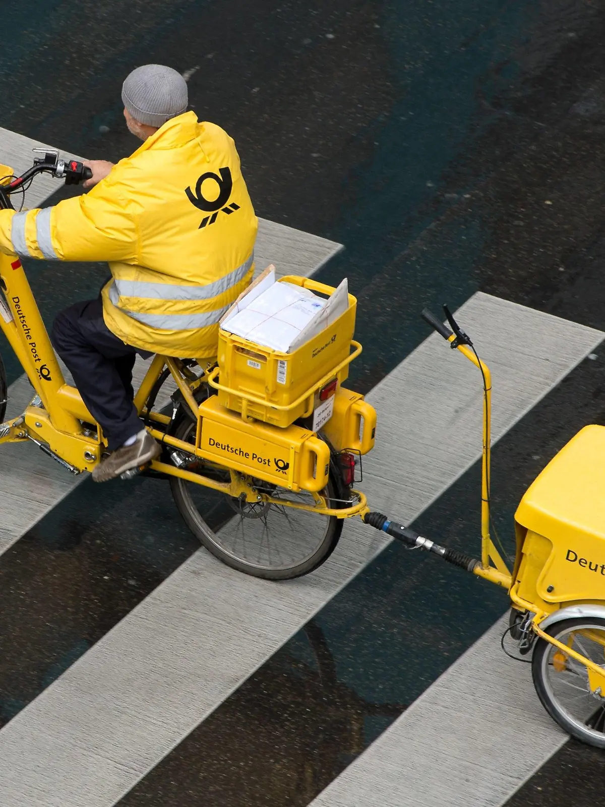 ARCHIV - 23.05.2014, Baden-Württemberg, Stuttgart: Ein Briefträger der Deutschen Post fährt mit einem Fahrrad (E-Bike) über einen Zebrastreifen. (zu dpa "Zeitung: Post zahlt bei neuer Postboten-Ausbildung hohes Gehalt" vom 22.04.2018) Foto: Sebastian Kahnert/dpa +++ dpa-Bildfunk +++