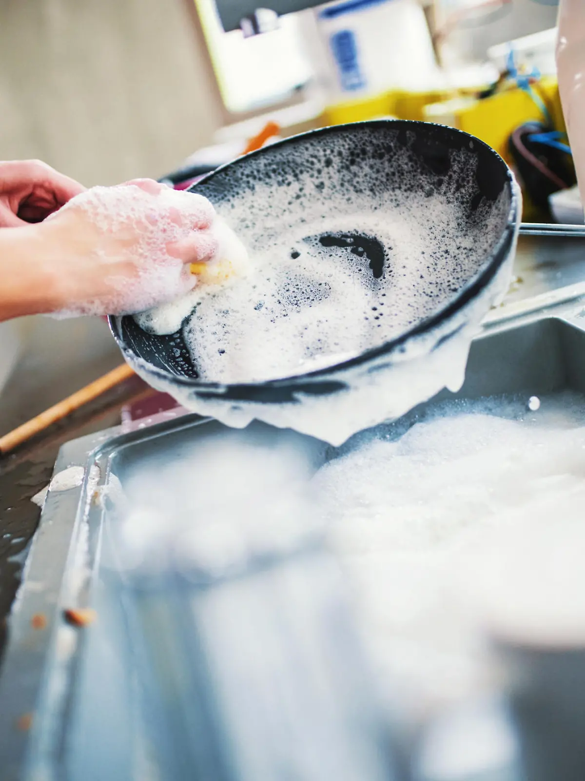 Closeup of unrecognizable woman doing dishes with lots of dirty plates and pots waiting aside. She's cleaning a black non stick cooking pan.