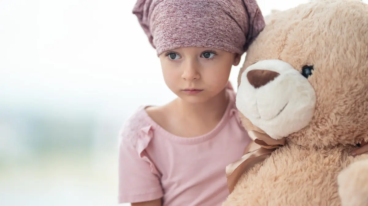 Kleines Mädchen mit Krebs kuschelt sich traurig an seinen Teddybär