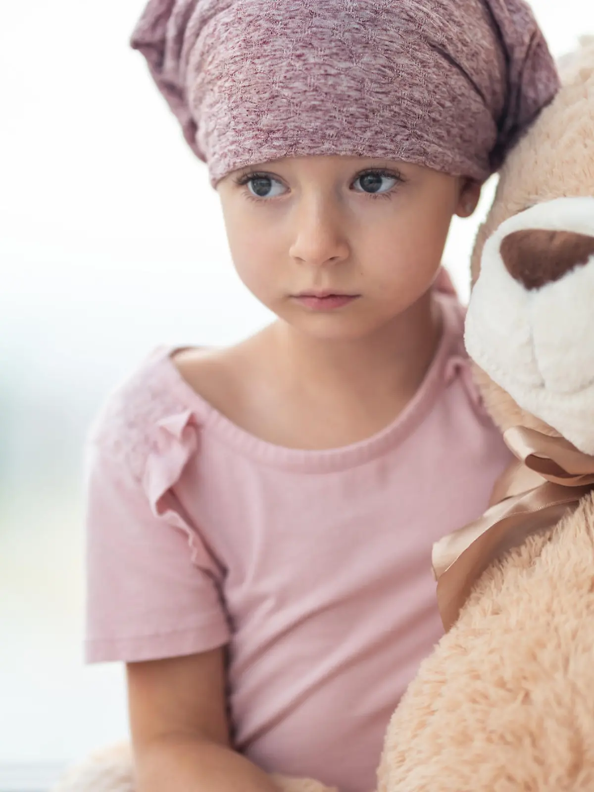 Kleines Mädchen mit Krebs kuschelt sich traurig an seinen Teddybär