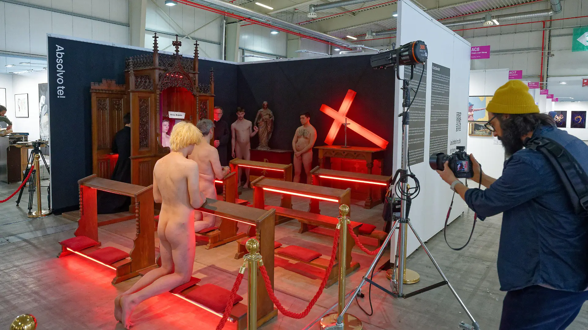 PRODUKTION - 20.04.2023, Nordrhein-Westfalen, Köln: Nackte Männer und zwei Männer in schwarzen Talaren agieren bei einer Kunstaktion. Bei der Inszenierung des Bonner Künstlers Dennis Josef Meseg auf der Discovery Art Fair Köln inszenieren sechs Aktmodelle «lebende Gemälde». Zur Kulisse gehört auch ein Beichtstuhl. Der Künstler will damit auf den Missbrauch in der katholischen Kirche und deren Umgang mit Tätern und Betroffenen aufmerksam machen. Foto: Henning Kaiser/dpa - ACHTUNG: Ein Teil des Bildes wurde aus rechtlichen Gründen gepixelt +++ dpa-Bildfunk +++