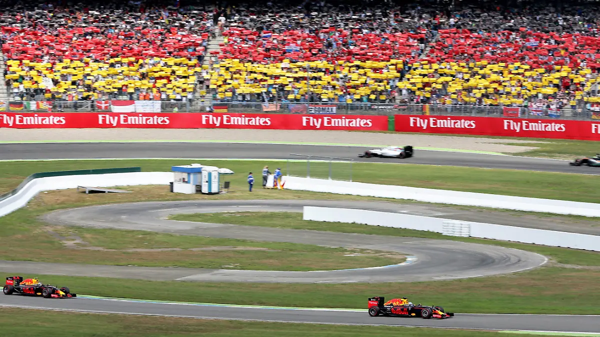 ARCHIV - 31.07.2016, Baden-Württemberg, Hockenheim. Der niederländische Formel-1-Rennfahrer Max Verstappen (r) und der australische Formel-1-Rennfahrer Daniel Ricciardo (beide Red Bull Racing) fahren beim Großen Preis von Deutschland auf dem Hockenheimring an einer schwarz-rot-goldenen Tribüne vorbei. (Zu dpa «Kein Heimspiel für Vettel 2019: Formel 1 umfährt Hockenheim» vom 27.06.2018) Foto: Jan Woitas/dpa +++ dpa-Bildfunk +++