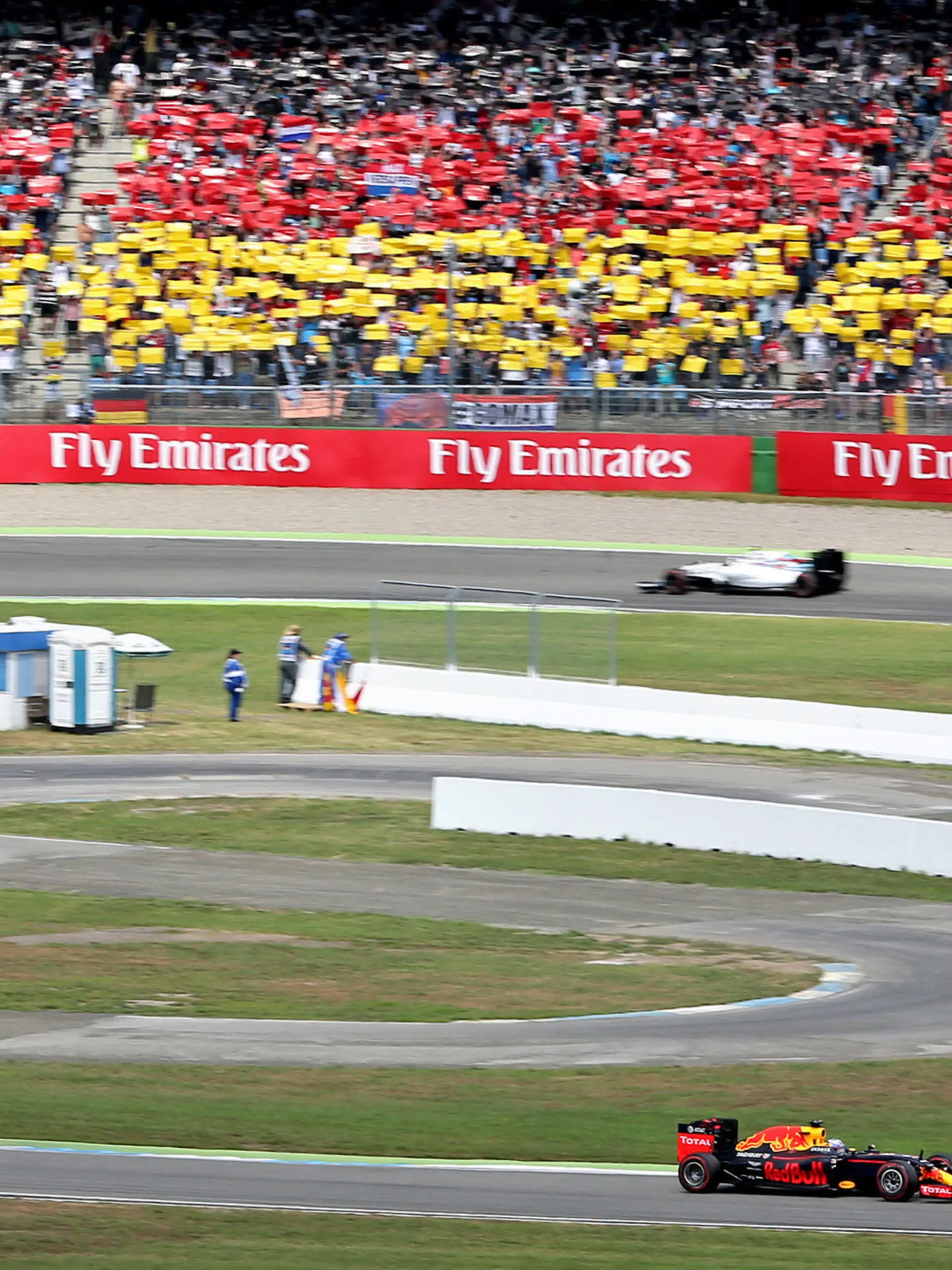 ARCHIV - 31.07.2016, Baden-Württemberg, Hockenheim. Der niederländische Formel-1-Rennfahrer Max Verstappen (r) und der australische Formel-1-Rennfahrer Daniel Ricciardo (beide Red Bull Racing) fahren beim Großen Preis von Deutschland auf dem Hockenheimring an einer schwarz-rot-goldenen Tribüne vorbei. (Zu dpa «Kein Heimspiel für Vettel 2019: Formel 1 umfährt Hockenheim» vom 27.06.2018) Foto: Jan Woitas/dpa +++ dpa-Bildfunk +++