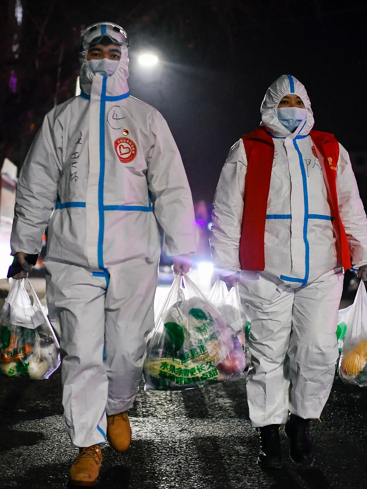 24.01.2021, China, Tonghua: Du Sicheng (l), ein Freiwilliger der Gemeinde Dongchang, und ein weiterer Helfer tragen Lebensmittel zu einer Wohngemeinschaft, deren Bewohner sich in Quarantäne befinden, in der Provinz Jilin im Nordosten der Volksrepublik China. Der 23-jährige Lehrer Du Sicheng, der in der Autonomen Region Tibet arbeitet, kehrte nach Beginn der Schulferien in seine Heimatstadt Tonghua zurück und schloss sich, nachdem seine Quarantäne am 23.01.2021 endete, den mehr als tausend Freiwilligen der Gemeinde an, um Menschen, die sich noch in Quarantäne befinden, mit Gütern des täglichen Bedarfs zu versorgen. Foto: Xu Chang/XinHua/dpa +++ dpa-Bildfunk +++