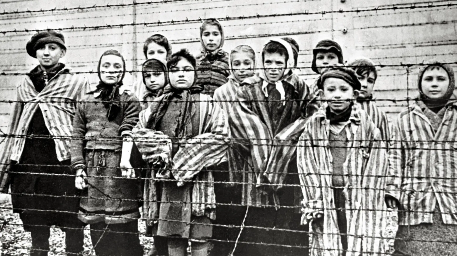 Überlebende jüdische Kinder in Auschwitz Mit Krankenschwester hinter Stacheldrahtzaun. Das Foto wurde von einem sowjetischen Fotografen während der Herstellung eines Films über Befreiung des Lagers gemacht. Die Kinder wurden von den Russen mit Kleidung von erwachsenen Gefangenen verkleidet. Auschwitz, Polen. Datum: Februar 1945 *** Surviving Jewish children in Auschwitz with nurse behind barbed wire fence. The photo was taken by a soviet photographer while making a film about liberation of the camp. The children were disguised by the Russians with clothes of adult prisoners. Auschwitz Poland. Date of February, 1945