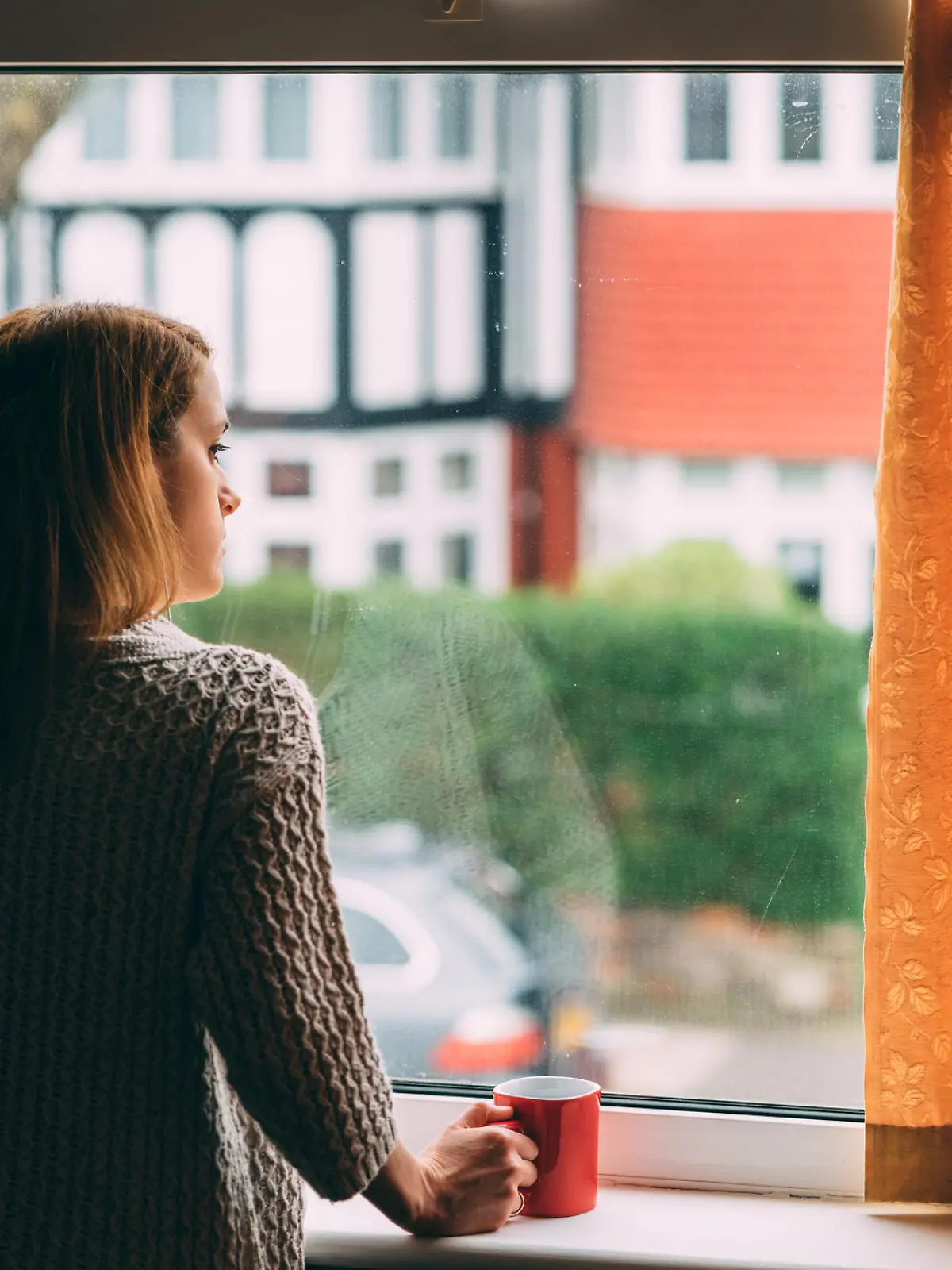 Frau steht am Fenster mit Tasse Kaffee in der Hand