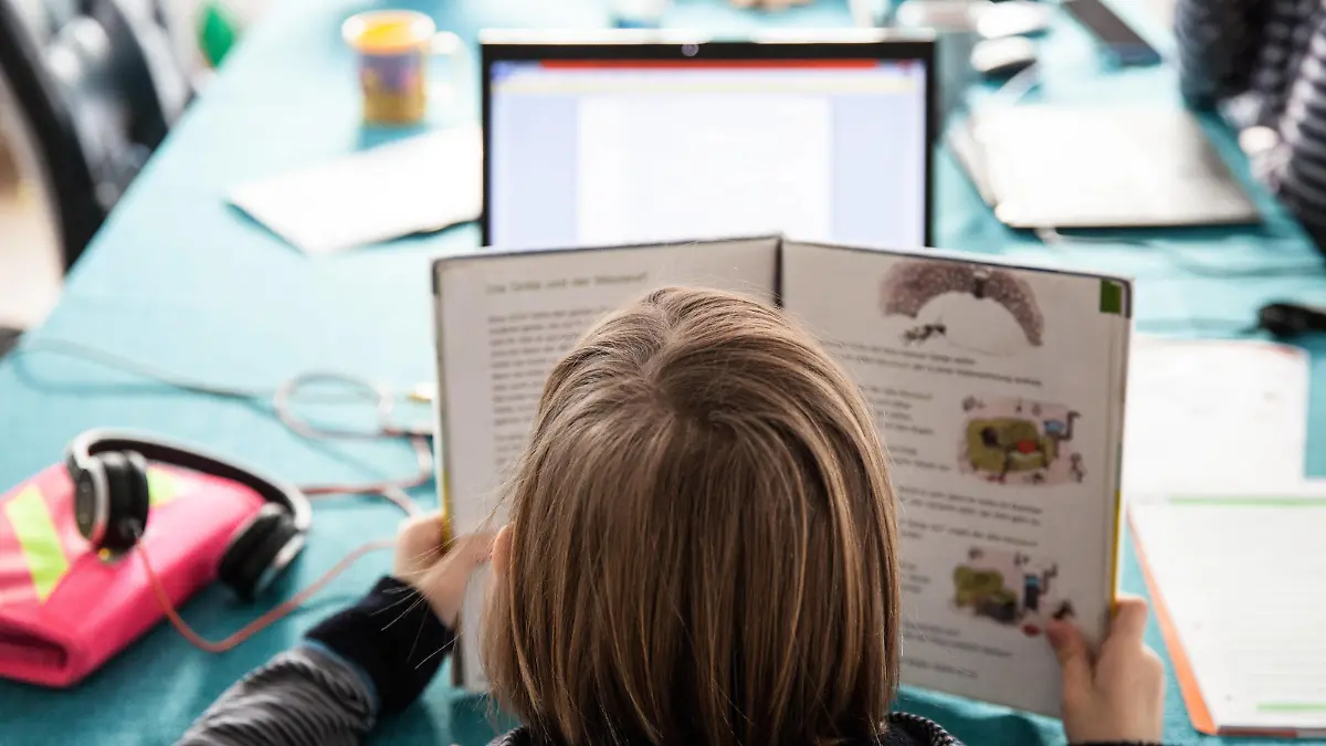 Bamberg, Deutschland 13. Januar 2021: Ein Schulkind hat ein Schulbuch in der Hand, sitzt an einem Tisch und macht Hausaufgaben im Homeschooling. Auf dem Tisch steht ein aufgeklappter Laptop für den Onlineunterricht. Bayern *** Bamberg, Germany 13 January 2021 A schoolchild holds a textbook, sits at a table and does homeschooling homework On the table is an unfolded laptop for online instruction Bavaria Copyright: xFotostandx/xK.xSchmittx
