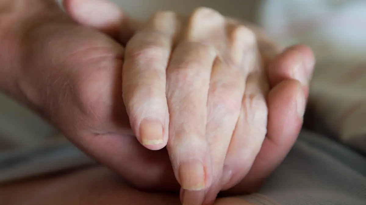 ARCHIV - 27.07.2015, --: Ein Altenpfleger hält in einem Pflegeheim die Hand einer Frau. (zu dpa ««Verabreichter Tod»? Streitthema Sterbehilfe treibt Frankreich um») Foto: Sebastian Kahnert/zb/dpa +++ dpa-Bildfunk +++