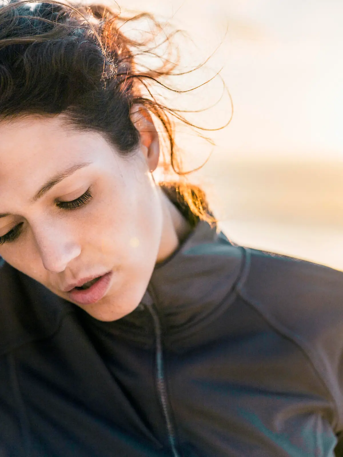 A photo of tired sporty woman looking down. Exhausted female athlete is wiping her forehead. She is wearing sportswear at beach.