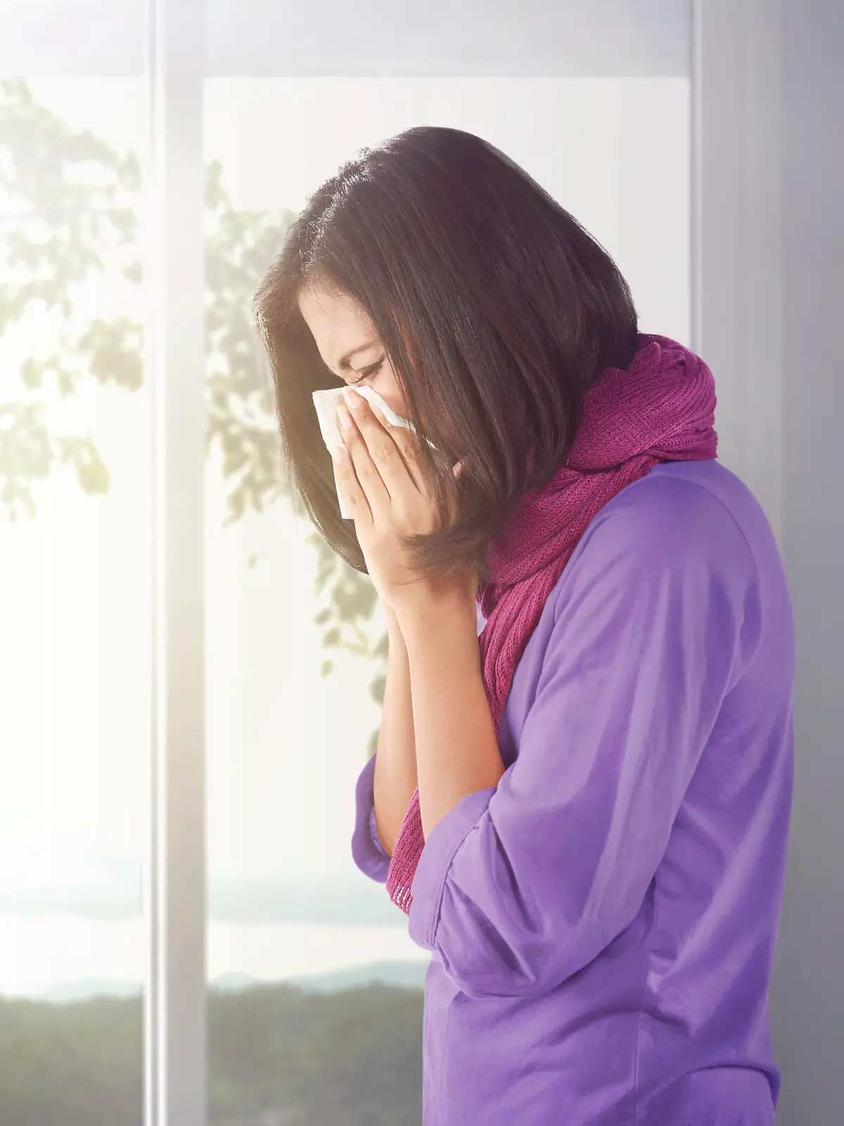 Sick asian woman holding a tissue in her nose at home