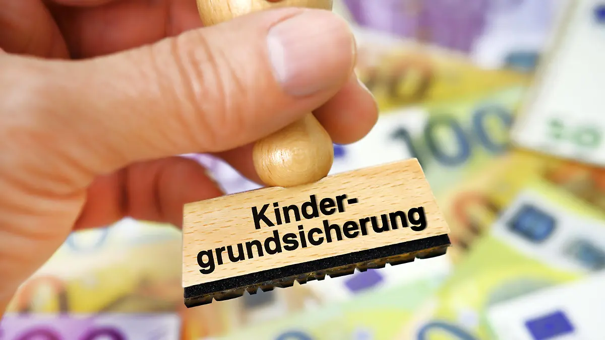 FOTOMONTAGE, Hand hält Stempel mit Schriftzug Kindergrundsicherung über Geldscheinen *** PHOTOMONTAGE, hand holding stamp with writing child basic security over banknotes