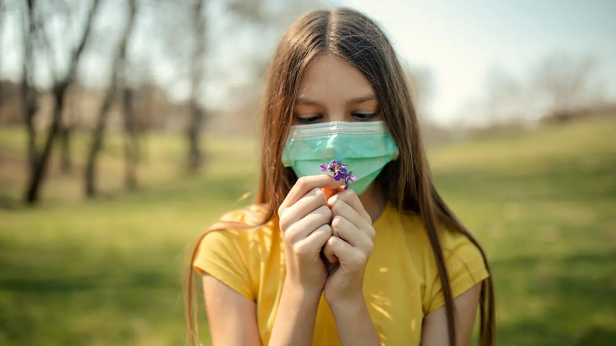 Frau mit Maske riecht an Blume