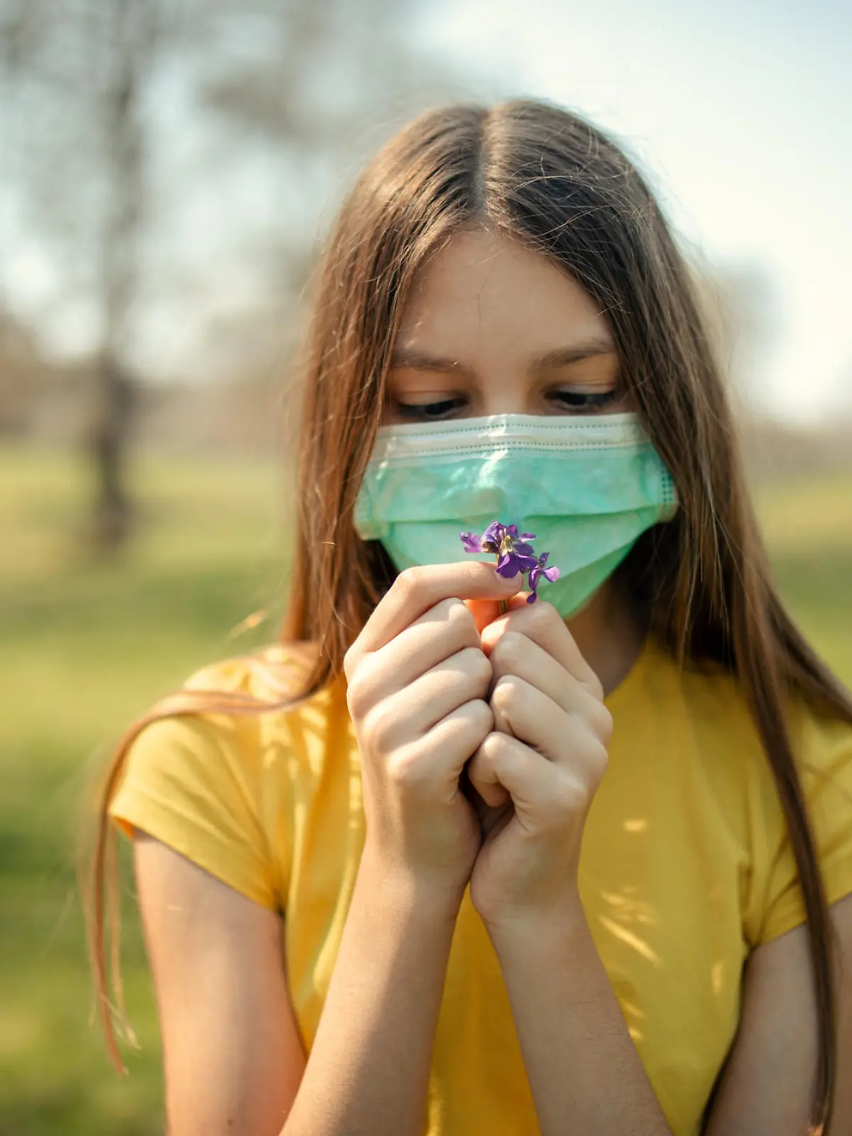 Frau mit Maske riecht an Blume
