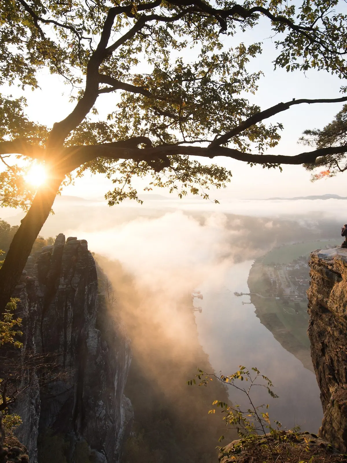 07.10.2019, Sachsen, Lohmen: Ein Mann hockt im Nationalpark Sächsische Schweiz auf dem Basteifelsen und fotografiert den Sonnenaufgang. Foto: Sebastian Kahnert/dpa-Zentralbild/dpa +++ dpa-Bildfunk +++