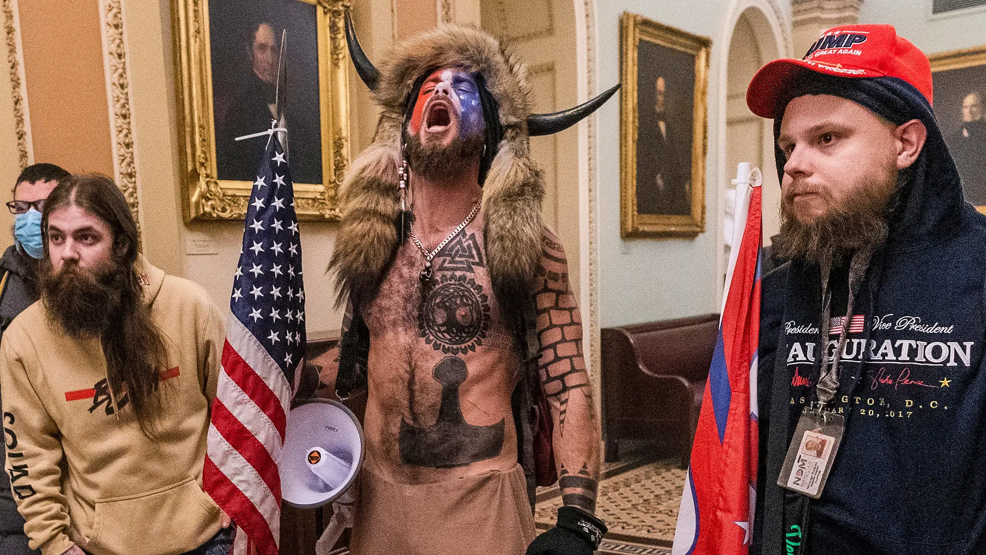 06.01.2021, USA, Washington: Unterstützer von US-Präsident Trump stehen auf dem Gang vor der Senatskammer im Kapitol. Unter den Eindringlingen in das US-Kapitol am Mittwoch in Washington sind auch Anhänger der rechten «QAnon»-Verschwörungstheorie gewesen. Vor allem Aufnahmen eines Aktivisten mit nacktem Oberkörper und einer Fellmütze mit markanten Büffelhörnern kursieren im Netz. Der «Schamane» war mit anderen bis in den Sitzungssaal des Senats vorgedrungen. (zu dpa ««QAnon»-Anhänger bei Kongress-Sturm in vorderster Reihe vertreten») Foto: Manuel Balce Ceneta/AP/dpa +++ dpa-Bildfunk +++