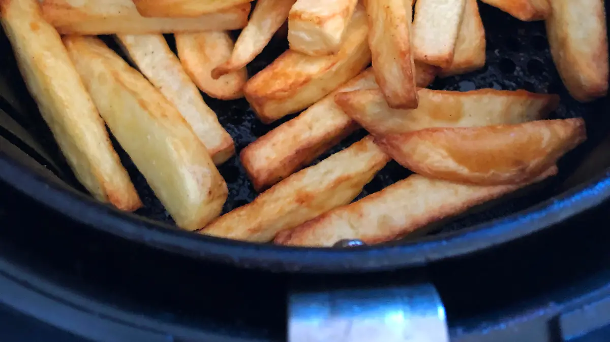 Stock photo showing the inside of an air fryer with a pile of golden brown, freshly cooked French fries / chunky chips. Healthy cooking concept.