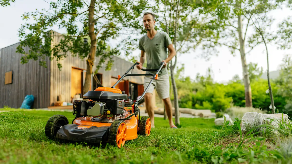 Photo of a young boy helping his father at mowing the lawn in their backyard