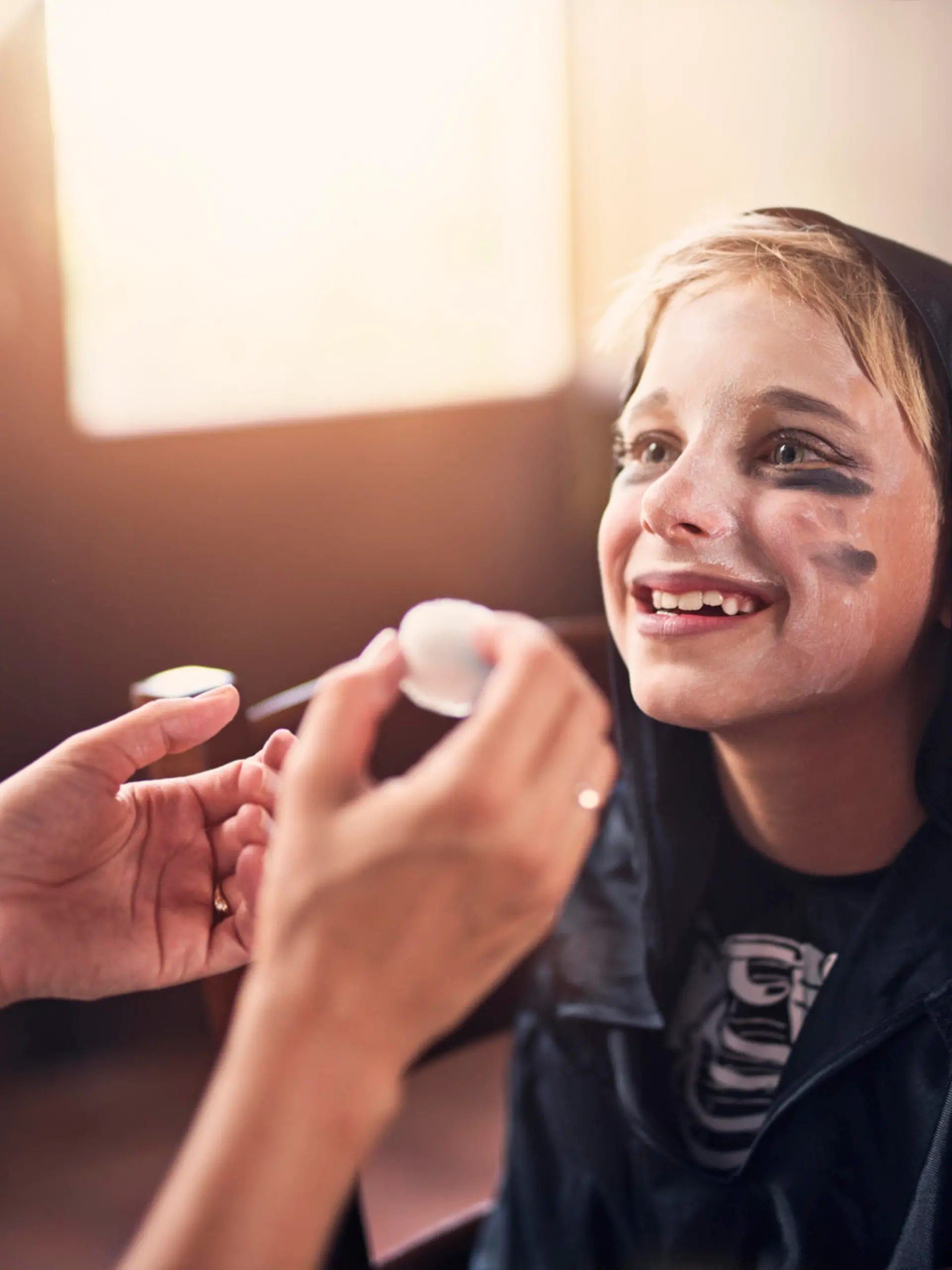 Little boy aged 8 preparing for halloween. Mother is painting the boy face and the boy is smiling at his mother.

