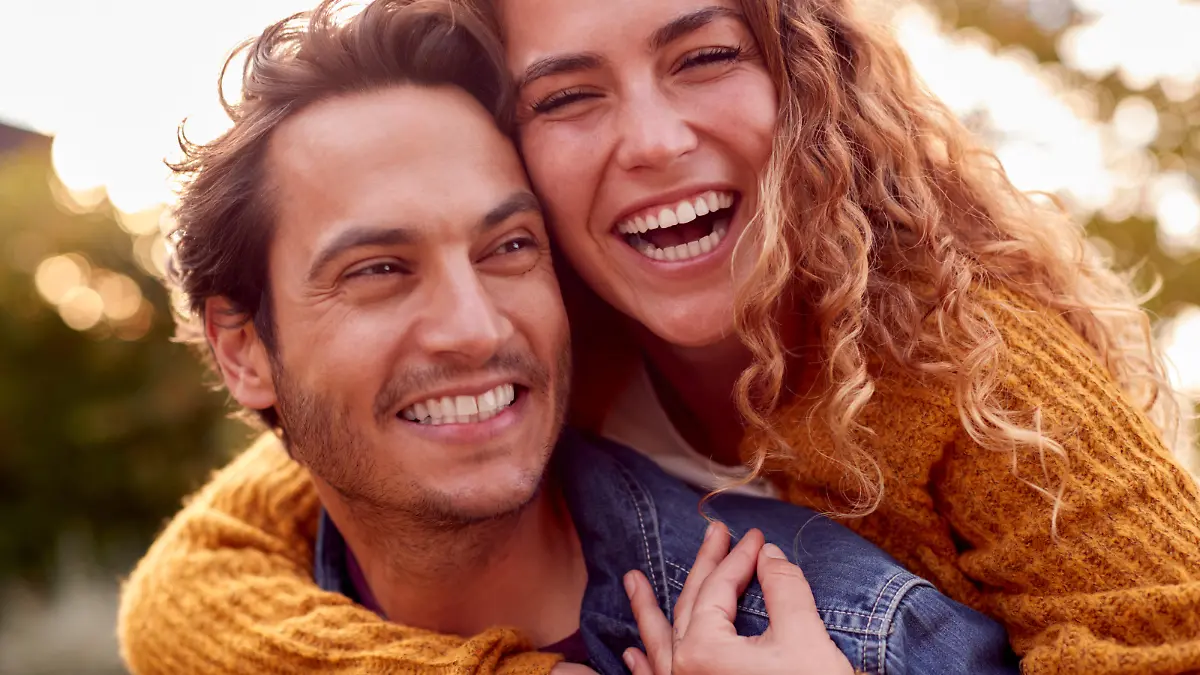 Portrait Of Happy Loving Couple With Man Giving Woman Piggyback As They Hug In Autumn Park Together