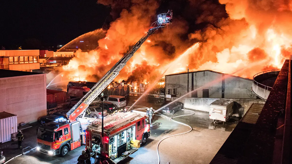 26.09.2021, Hamburg: Feuerwehrleute löschen im Stadtteil Rothenburgsort einen Großbrand. Auf einem Industriegelände sind in der Nacht vermutlich Sperrmüll und Elektrogeräte in Brand geraten, anschließend griff das Feuer auf eine Lagerhalle über. (zu dpa «Brand einer Lagerhalle in Hamburg - große Rauchsäule am Himmel») Foto: Daniel Bockwoldt/dpa +++ dpa-Bildfunk +++