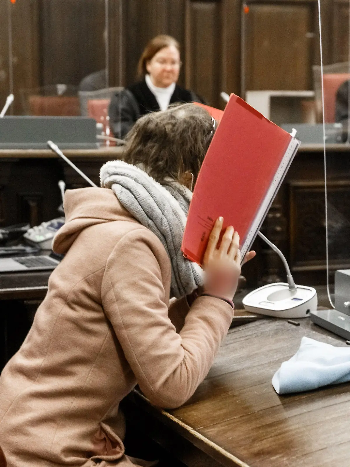 23.12.2020, Hamburg: Die 37-jährige Angeklagte (vorne) sitzt im Gerichtssaal neben ihrem Anwalt und verbirgt ihr Gesicht hinter einem Aktendeckel im Prozess wegen Mordes an ihrem 80-jährigem Ex-Freund. Der Angeklagten wird vorgeworfen, im April ihren ehemaligen Lebensgefährten aus Habgier getötet zu haben. Heute wird ein Urteil erwartet. Foto: Markus Scholz/dpa Pool/dpa - ACHTUNG: Ein Tattoo auf der Hand wurde aus rechtlichen Gründen gepixelt +++ dpa-Bildfunk +++