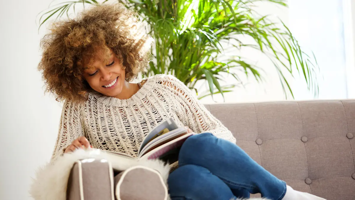 Portrait of attractive african american woman sitting on sofa reading book
